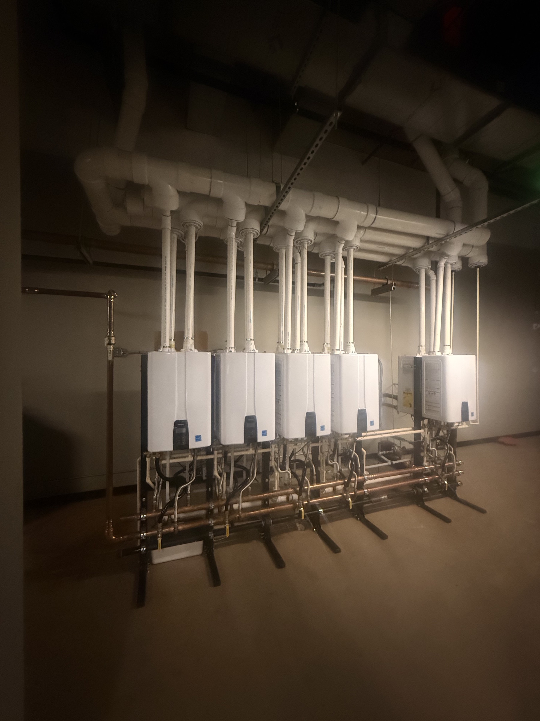 Bank of tankless water heaters installed with copper piping and overhead venting.