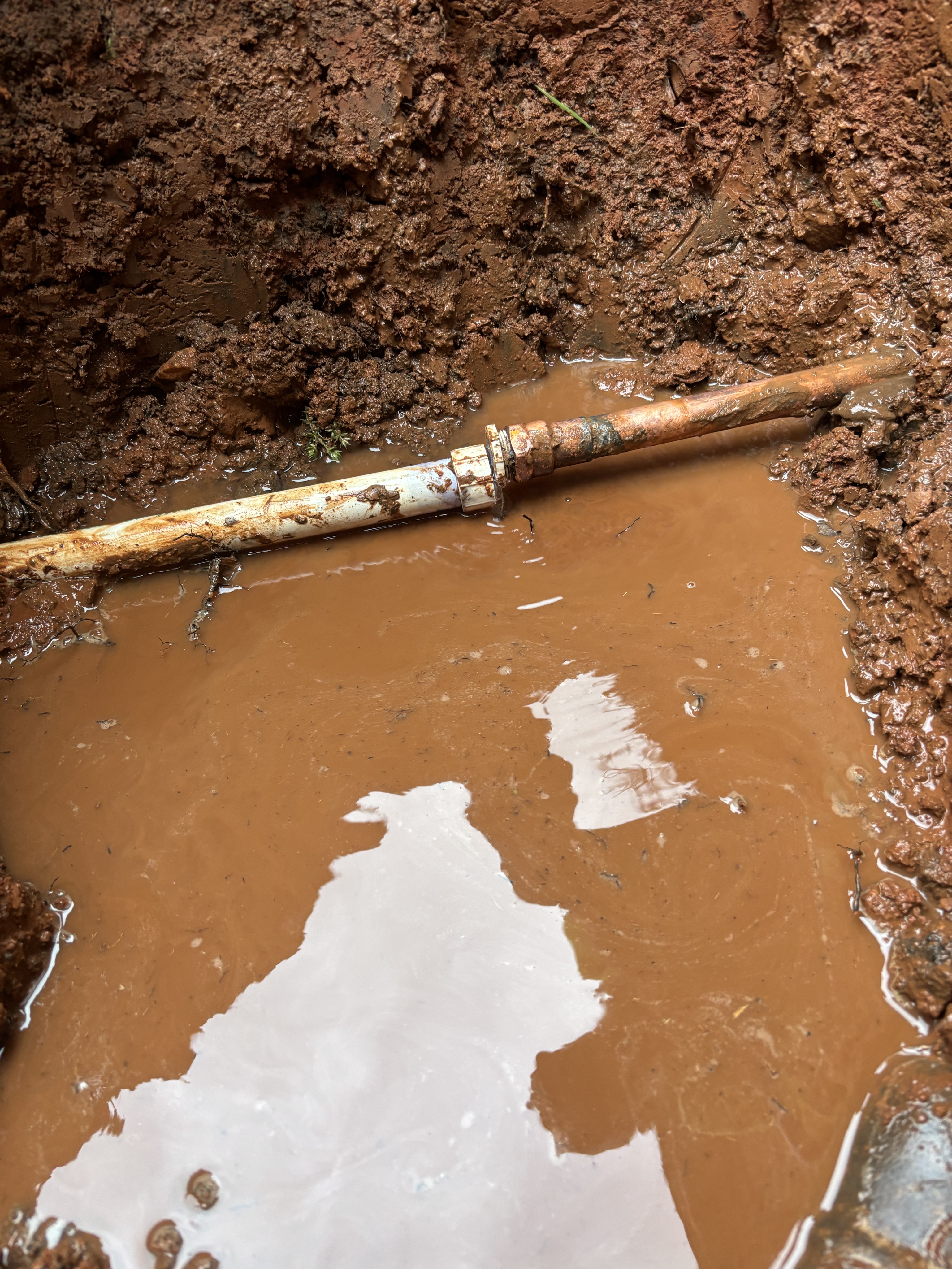Exposed service-line connection in a residential excavation.