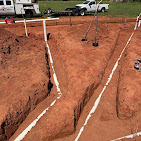 New construction plumbing rough-in with pipe runs in red dirt.