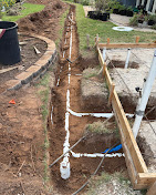 Residential yard trench with white plumbing pipe installed.