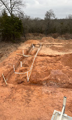 Plumbing lines set in open red dirt trenches.