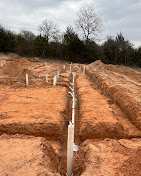 Underground plumbing rough-in installed in a red dirt trench.